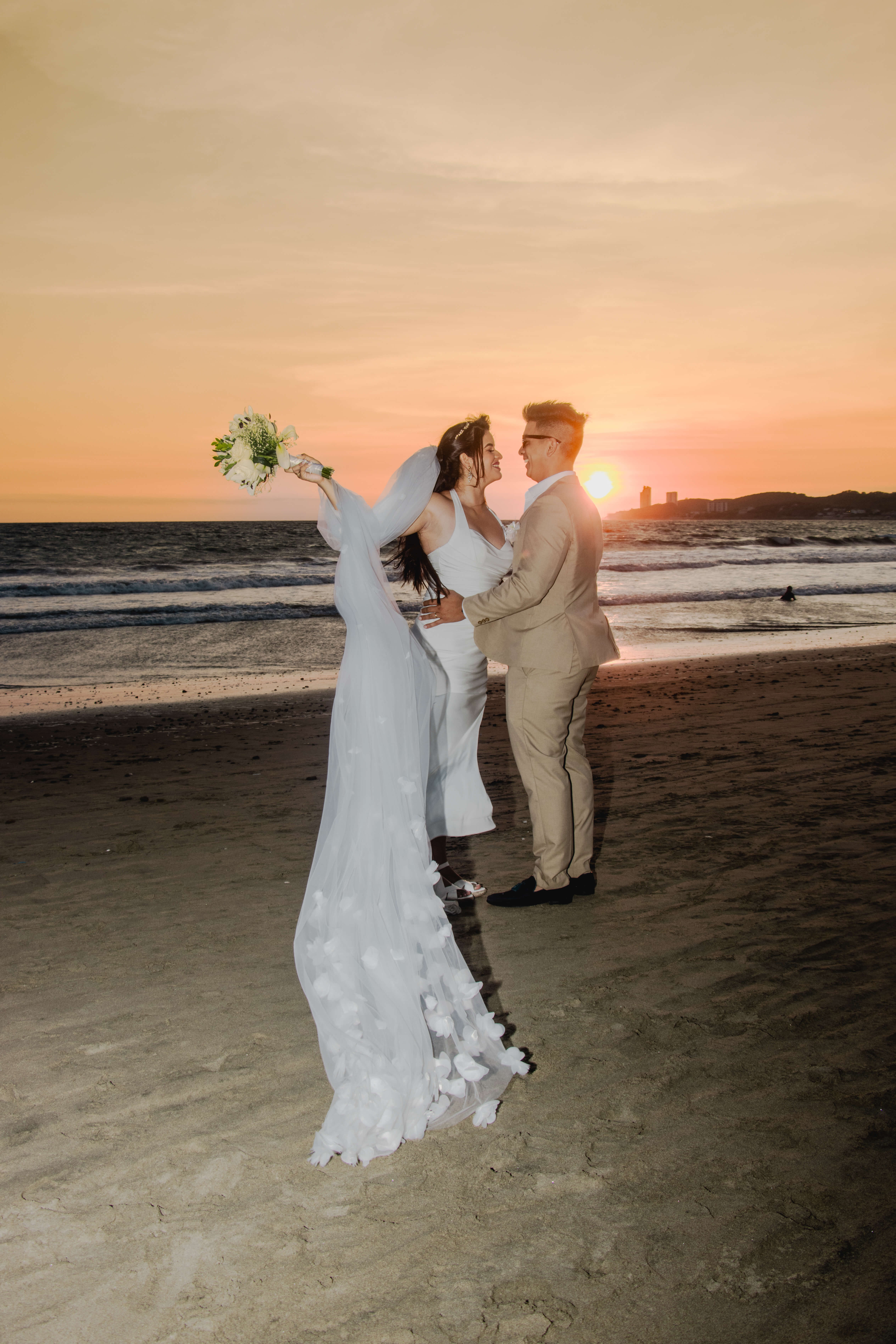 La pareja de novios se abraza al atardecer en General Villamil Playas, rodeados de la tranquilidad del océano y la belleza de la naturaleza.